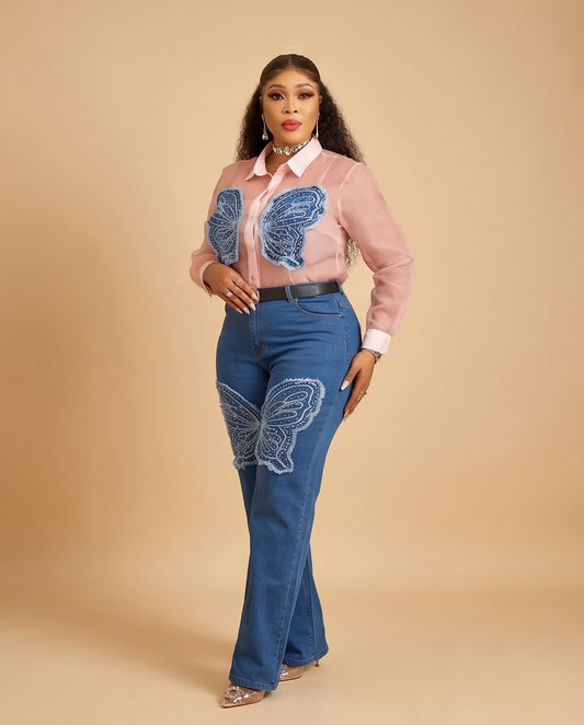 A woman modeling a pink long-sleeve button-up shirt with blue butterfly appliques and blue jeans with white butterfly appliques, set against a solid beige studio background.