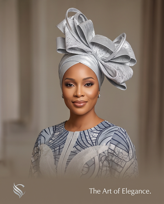 A woman wearing an elegant silver headwrap with a large bow and a matching patterned blue and white top, set against a soft beige background with the text 'The Art of Elegance.' at the bottom.