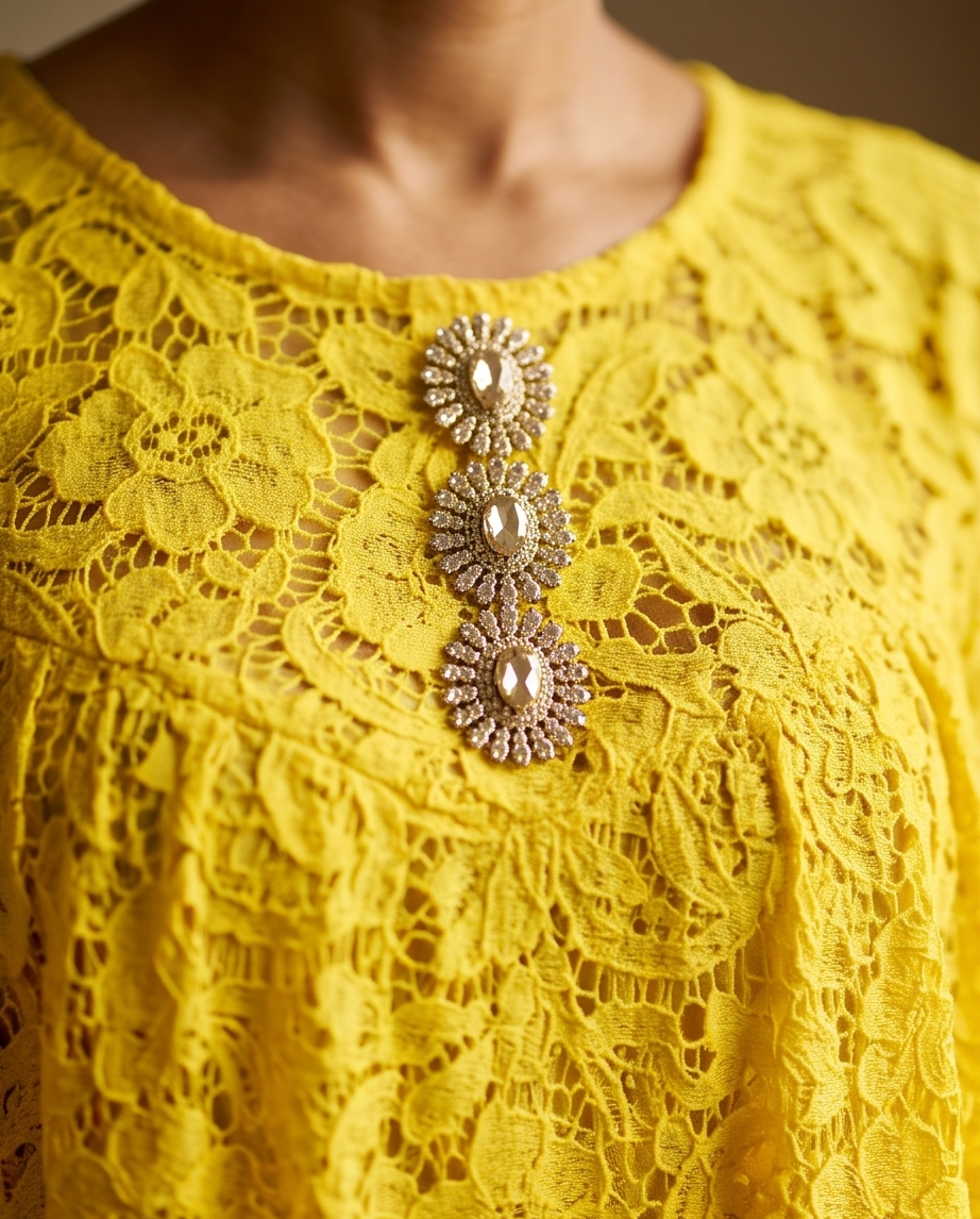 A close-up of a bright yellow lace top featuring three ornate gold-toned brooch embellishments on the chest.