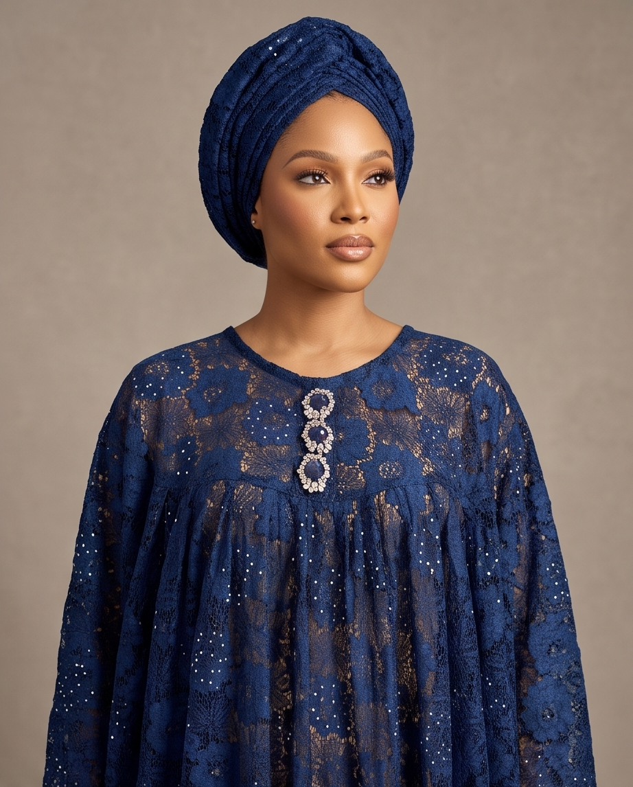 A woman wearing a deep blue lace dress with a matching blue headwrap, photographed against a neutral beige studio background.