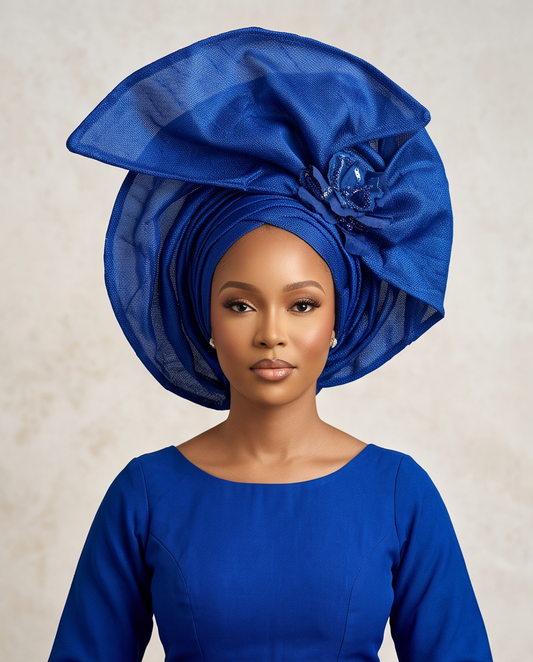 A woman wearing an elaborate royal blue headwrap and matching blue dress, photographed against a soft beige textured background.