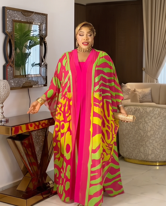 A woman models a vibrant magenta and lime green patterned kaftan dress in a modern, upscale living room setting.