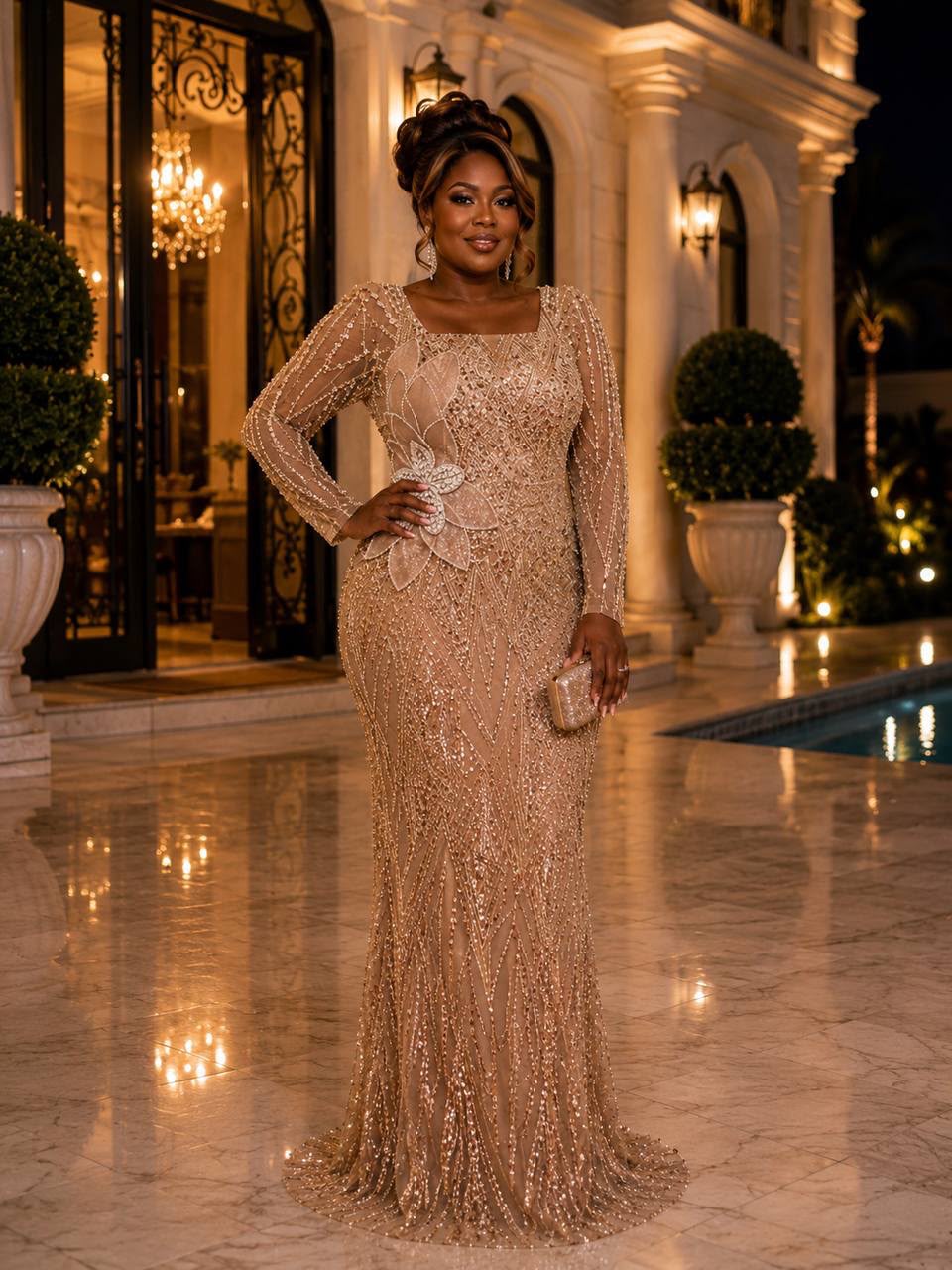 A woman stands outdoors in front of a grand illuminated building and pool, wearing a floor-length beige sequined gown with long sheer sleeves, a square neckline, and a fitted mermaid silhouette. She holds a small matching clutch.